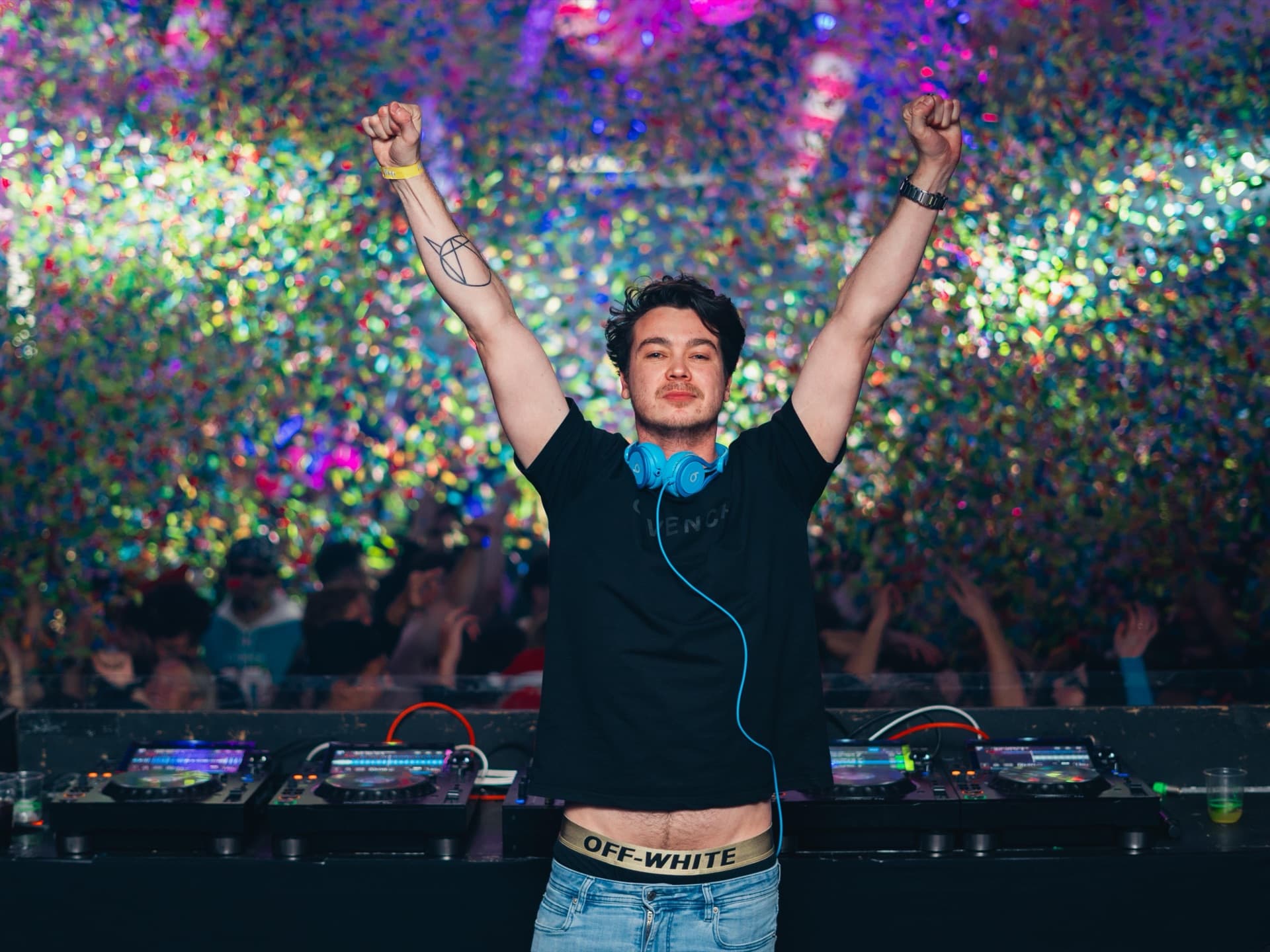 A DJ with both arms raised in front of a glitter wall at Ivy Thursdays