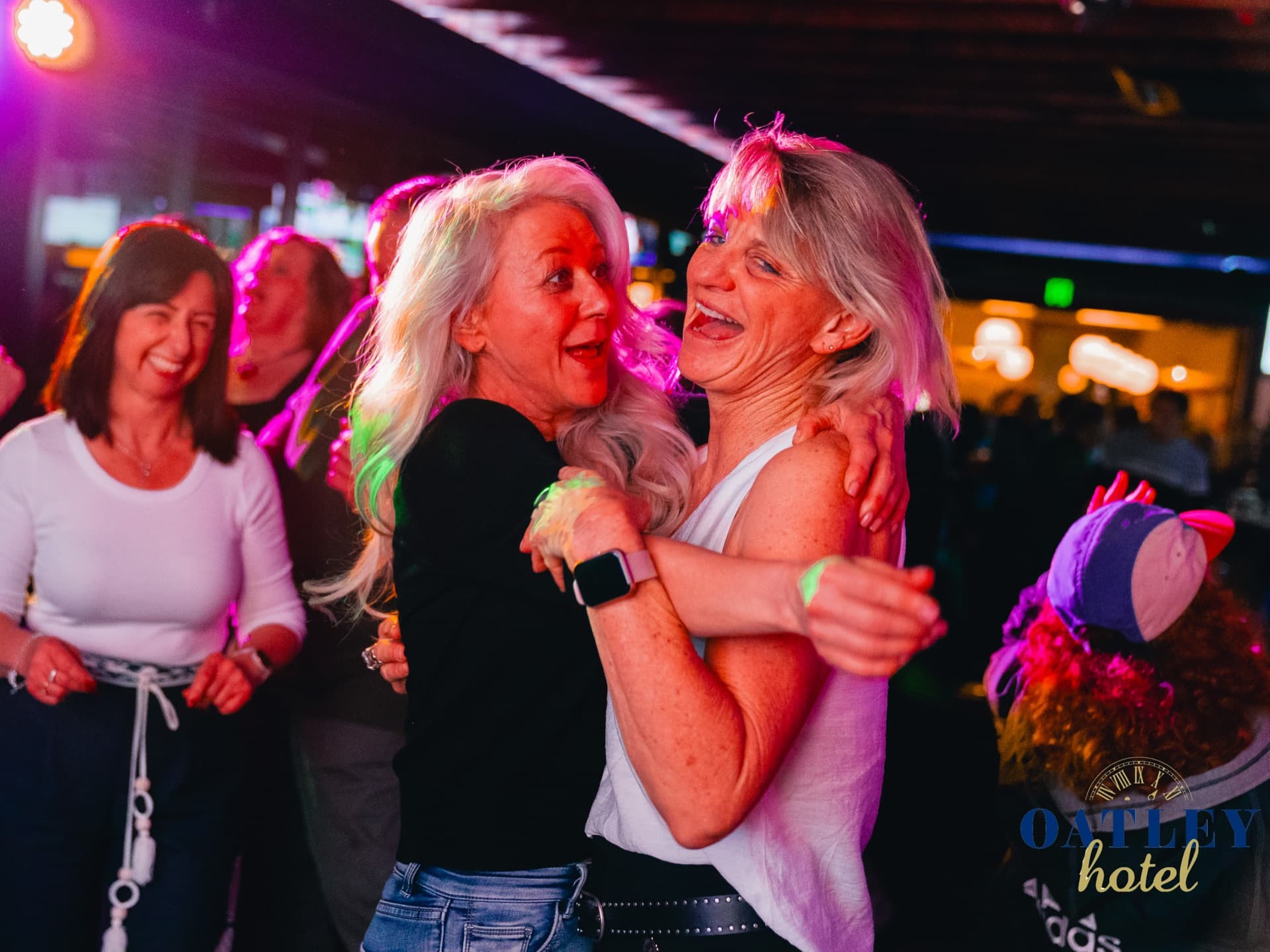 Two women dancing and laughing under purple light