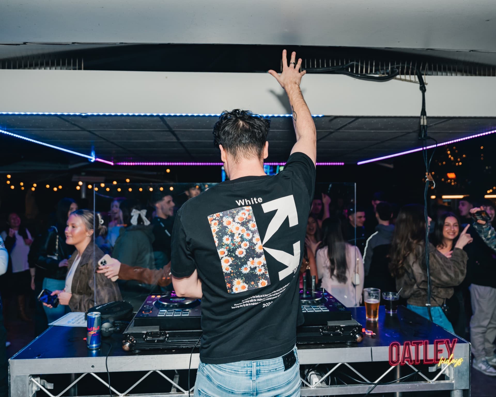 A DJ with one arm raised facing a packed room