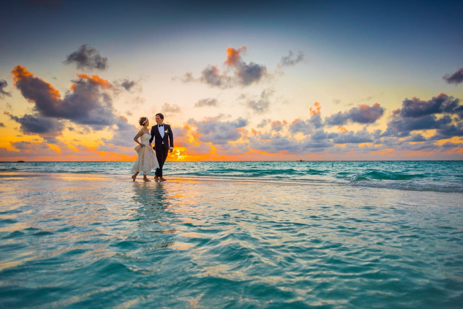 A couple walking through shallow water at sunset